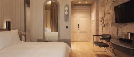 Habitación de hotel con una cama, una silla, un televisor montado en la pared y una puerta que da a otra habitación.