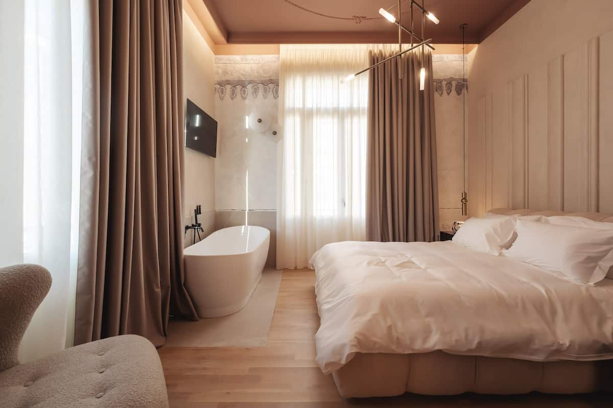 Un dormitorio moderno con una cama grande, una bañera y suelo de madera.