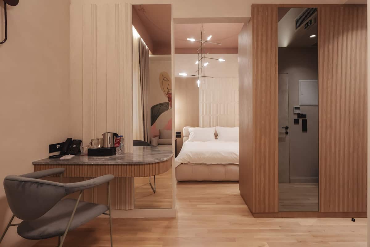 Una habitación de hotel moderna con piso de madera, una mesa de comedor redonda con sillas, una cama con ropa de cama blanca y un área de baño separada.