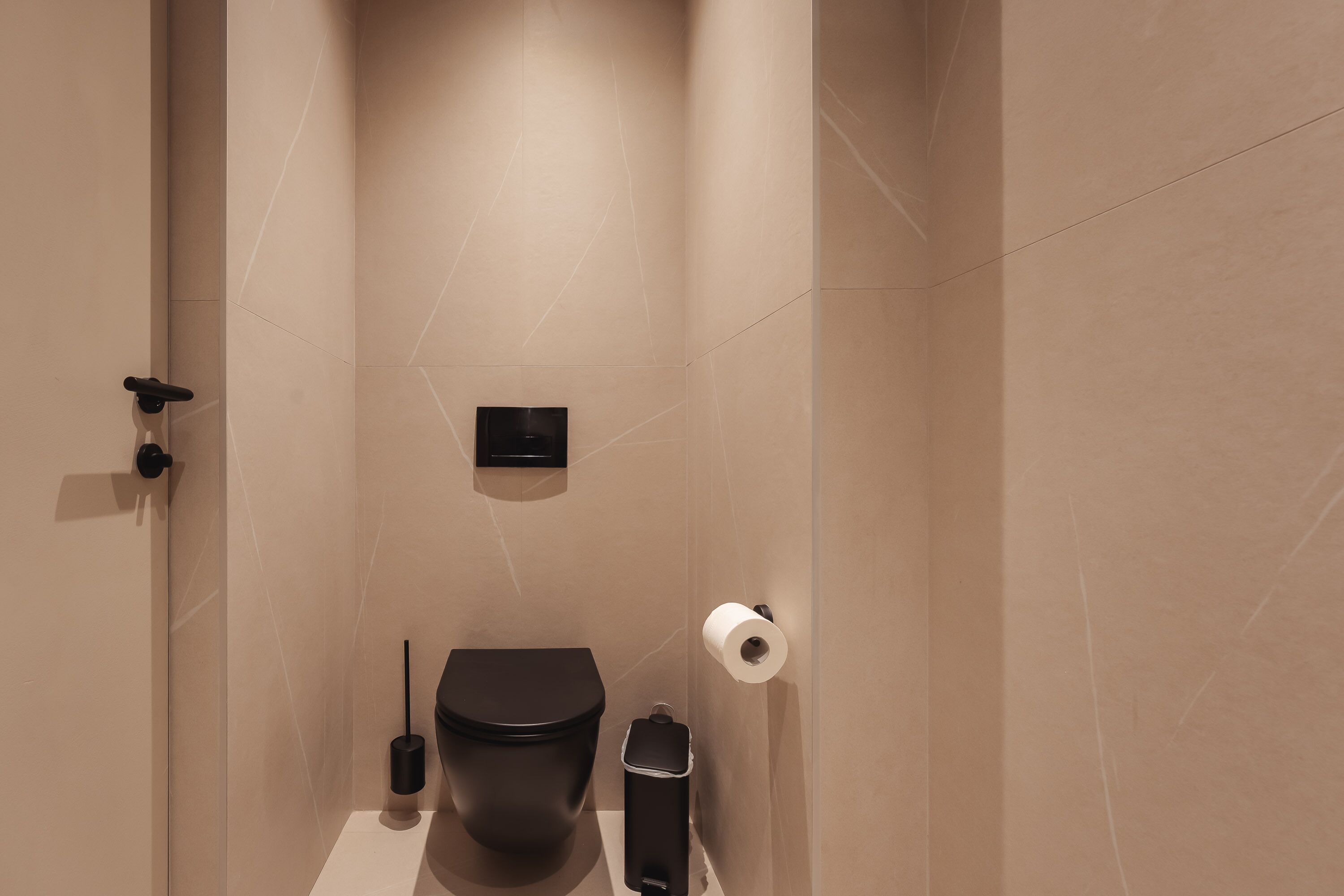 A modern bathroom with a toilet, a trash bin, and a toilet paper holder on the wall.