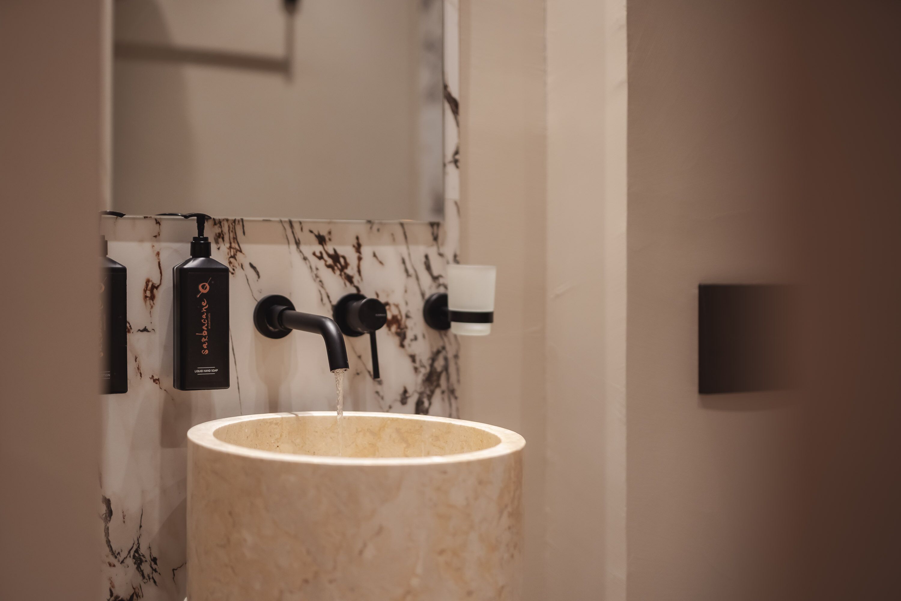 A bathroom with a marble sink, a black soap dispenser, and a towel dispenser.