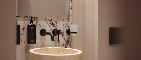 A bathroom with a marble sink, a black soap dispenser, and a towel dispenser.
