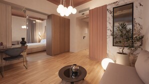 A modern hotel room with a wooden floor, a round table with a decorative item, a sofa, a large mirror, and a potted plant.