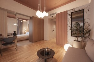 A modern hotel room with a wooden floor, a round table with a decorative item, a sofa, a large mirror, and a potted plant.