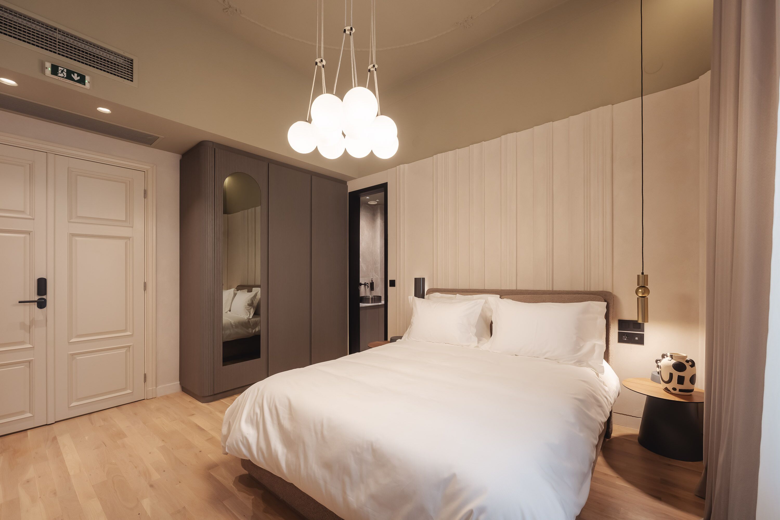 A modern bedroom with a large bed, a wardrobe, a mirror, and a unique ceiling light fixture.