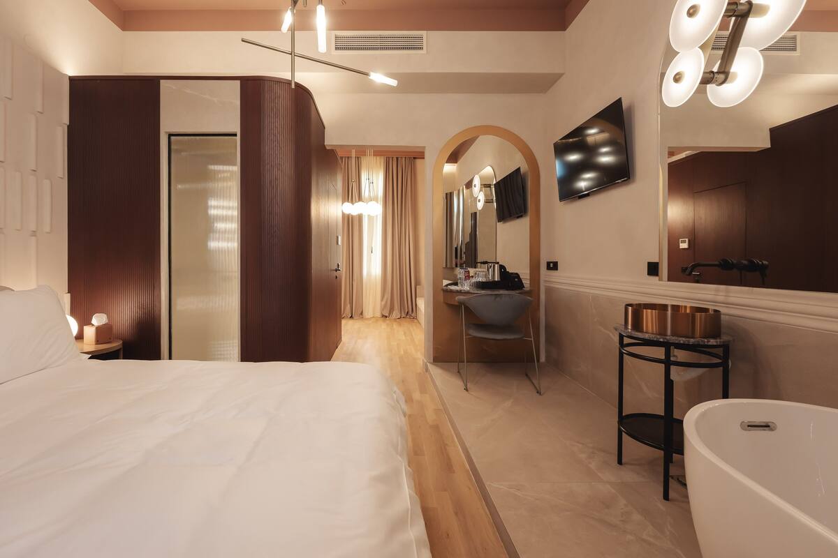 Una habitación de hotel moderna con una cama grande, un tocador con espejo, un lavabo y una bañera.