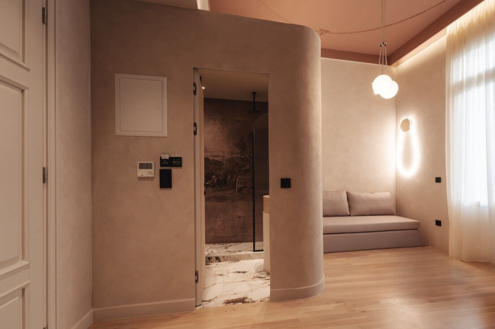 A modern interior with a curved wall, a wooden floor, a sofa, and a hanging light fixture.