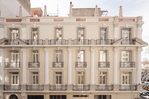 A multi-story building with a classical architectural style, featuring symmetrical windows, ornate balconies, and a central entrance.