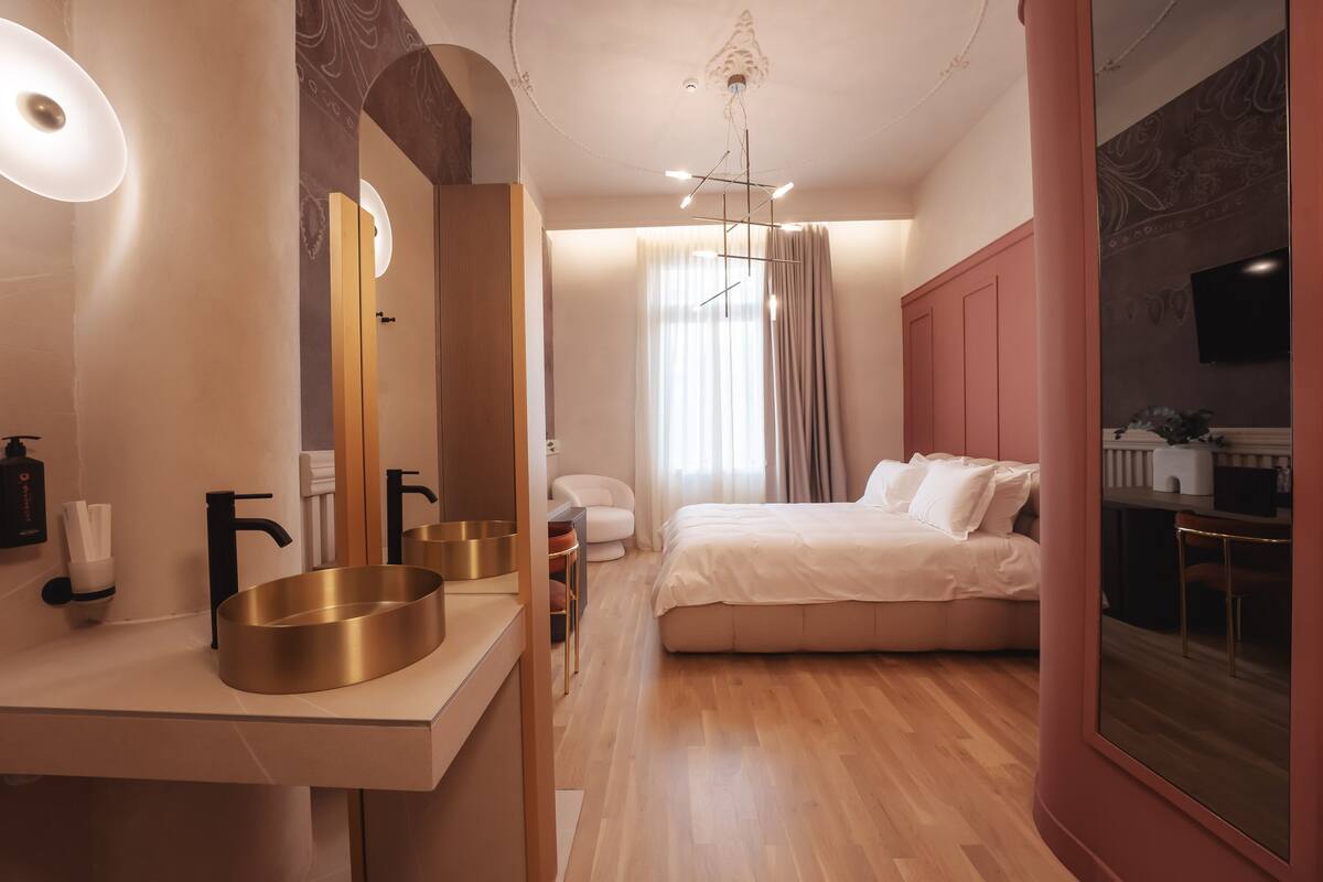 Un dormitorio moderno con una cama grande, un tocador con lavabo dorado, un espejo y una lámpara en el techo.