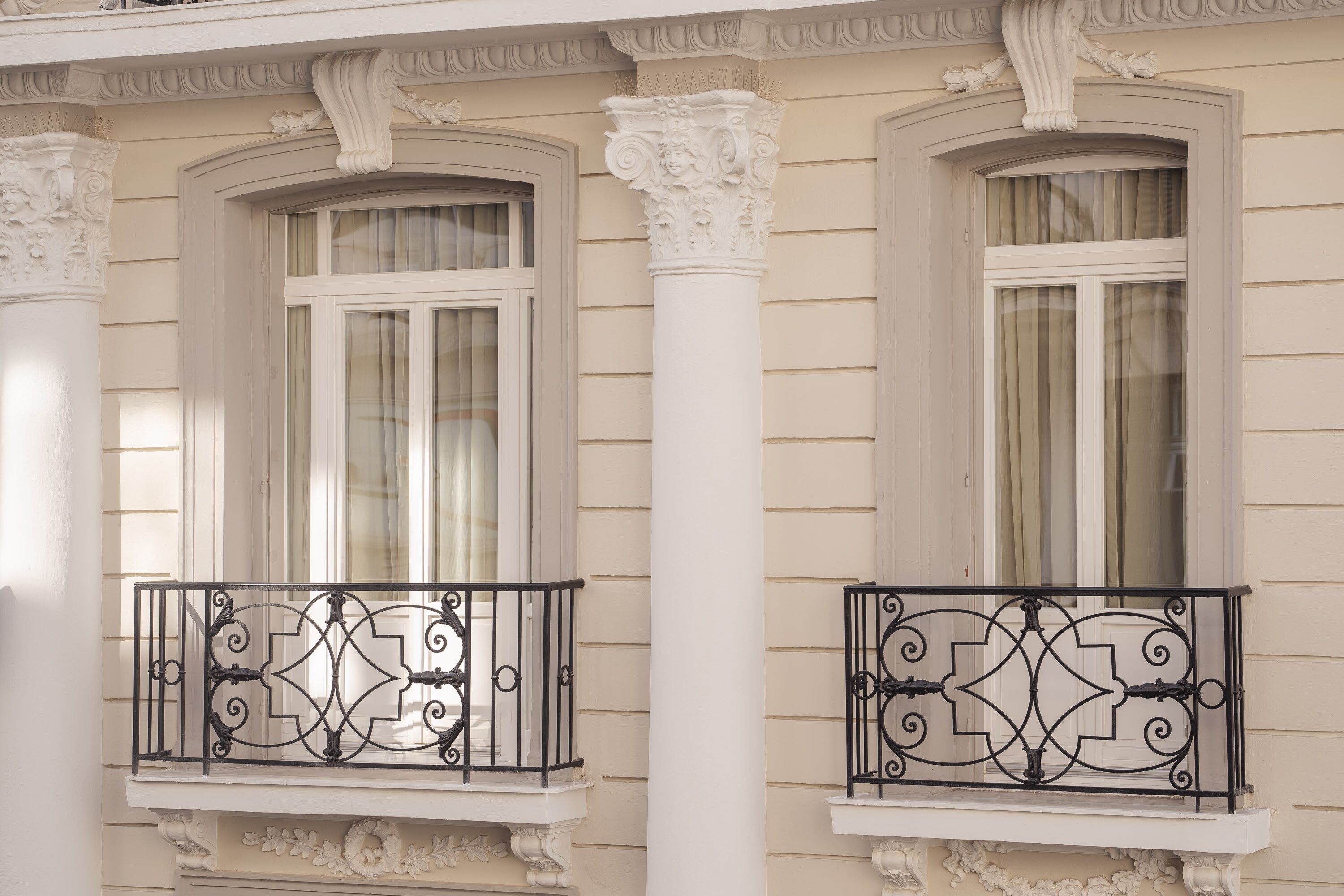 Egy épület homlokzata, melyen két ablak található, és mindkettőhöz tartozik egy-egy balkon, melyek díszes, fekete színű, fém korláttal vannak ellátva.