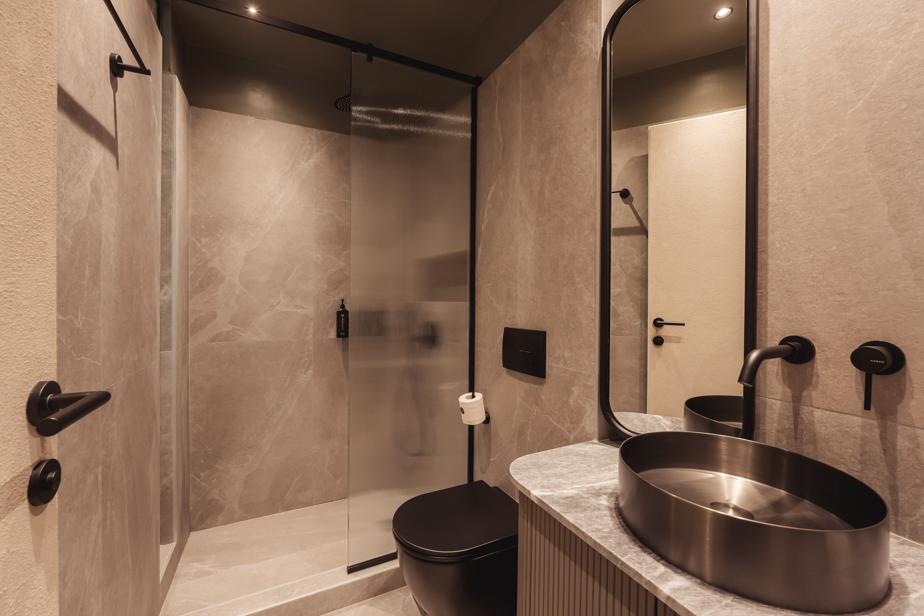 Un baño moderno con ducha de vidrio, un espejo grande y un lavamanos de acero inoxidable.