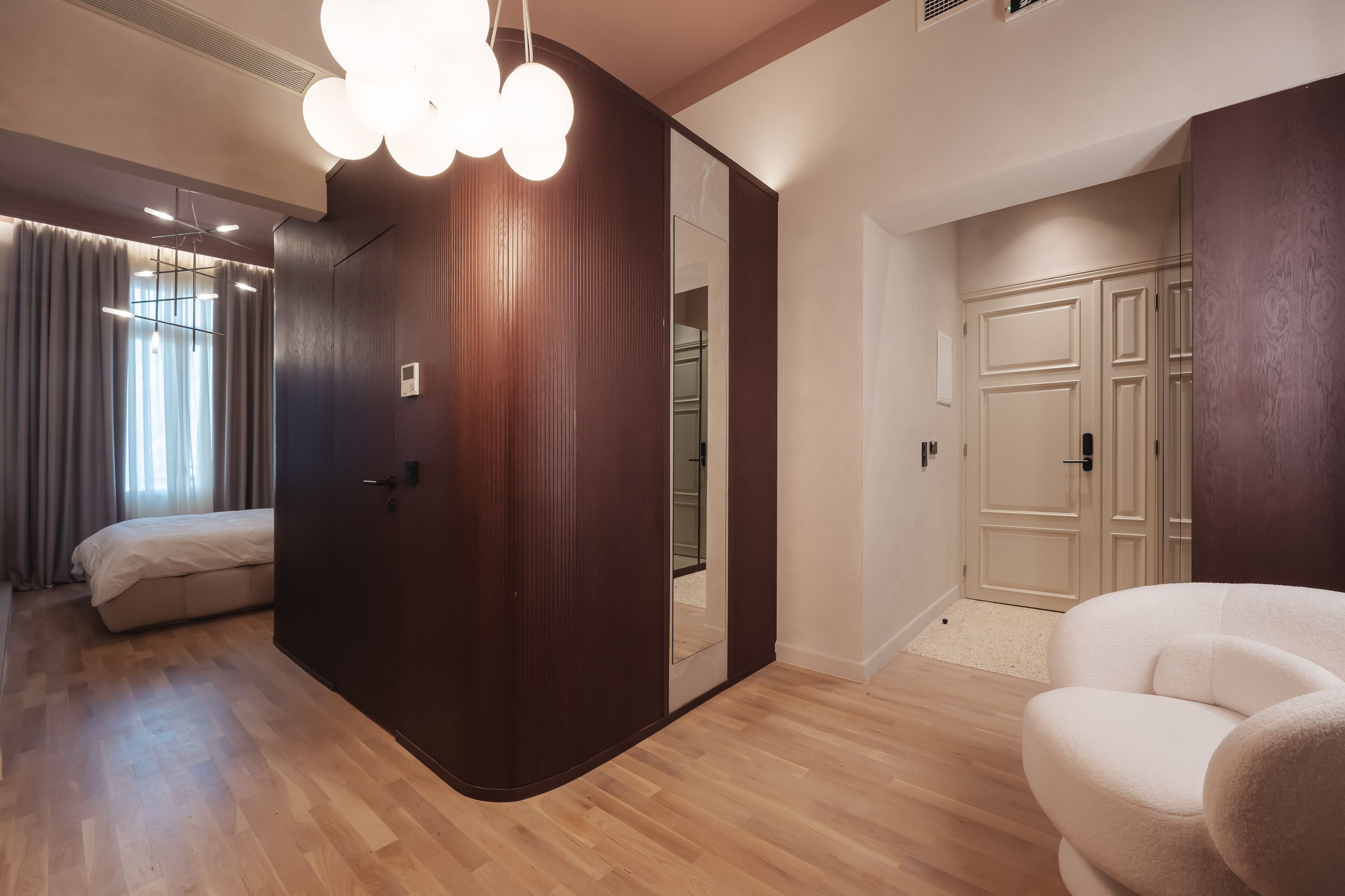 A modern bedroom with a wooden wardrobe, a large mirror, and a plush white chair.
