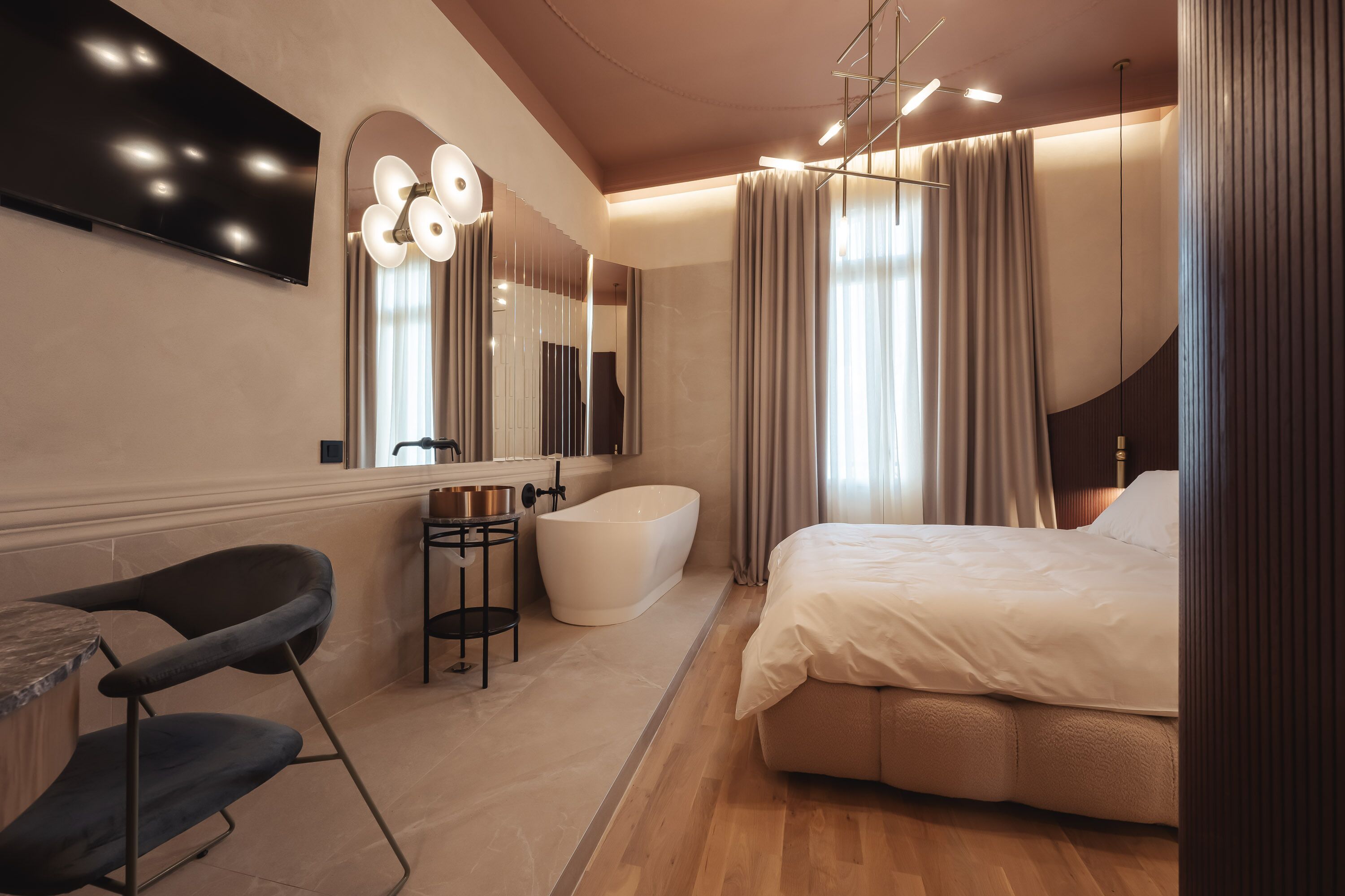 Un dormitorio moderno con una cama grande, un tocador con espejo, una bañera y un área de descanso con una silla y una mesa.