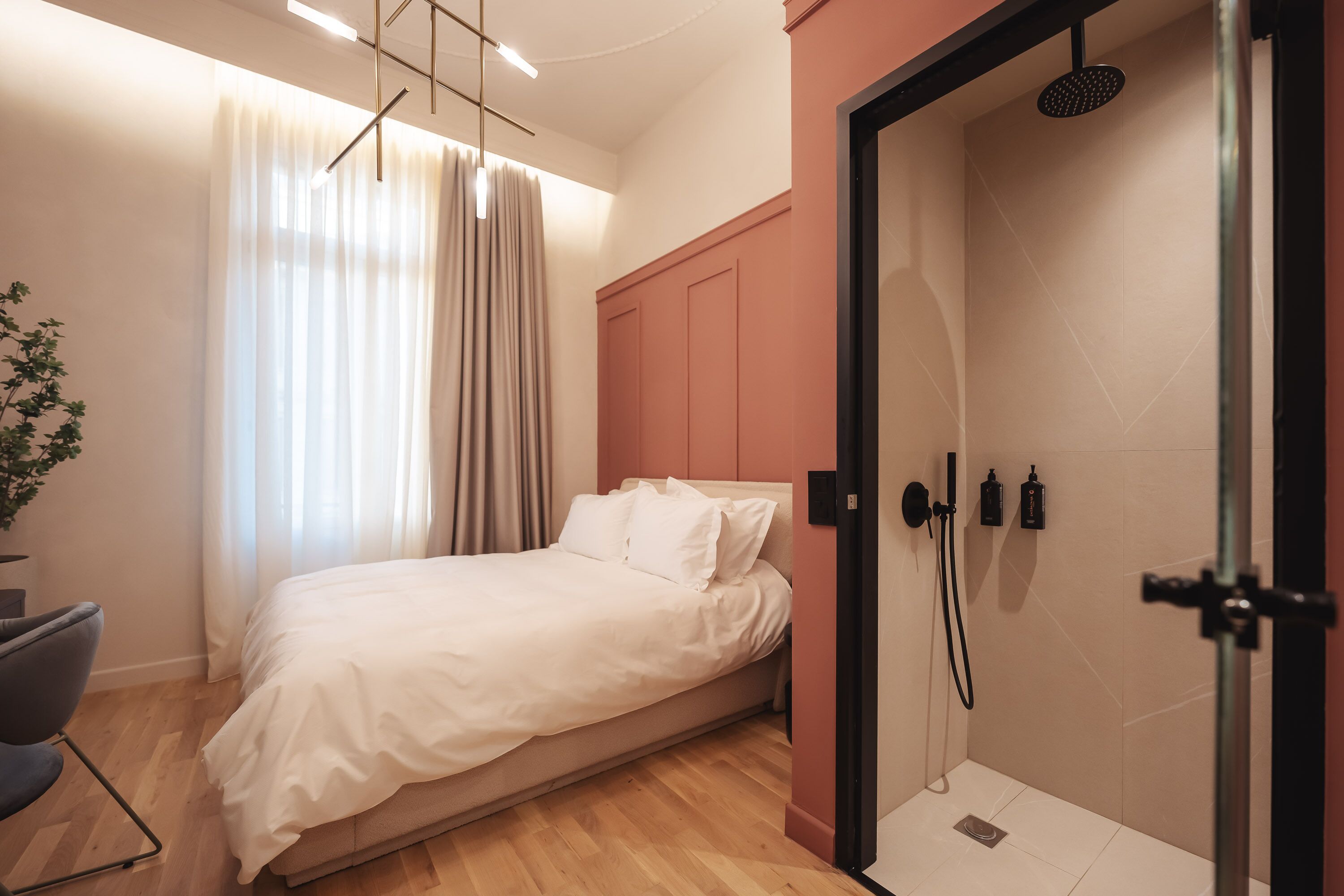 A modern bedroom with a bed, a shower area, and a potted plant.