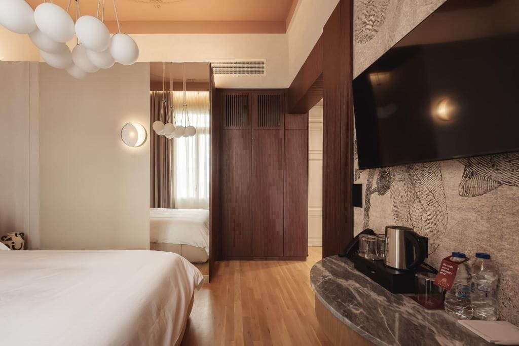 A modern hotel room with a bed, a wooden floor, a marble countertop with a coffee maker, and a flat-screen TV mounted on the wall.