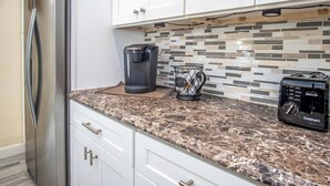 A kitchen with white cabinets, a stainless steel refrigerator, a coffee maker, a toaster, and a tiled backsplash. - Little Venice Family Affair 2 bedroom 1 bath One Block from the Ocean (Marathon)