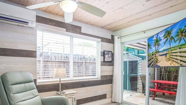 A room with a large window, a ceiling fan, a view of a beach through a glass door, and a light-colored floor. - Little Venice Family Affair 2 bedroom 1 bath One Block from the Ocean (Marathon)