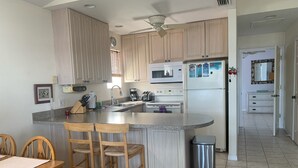 A kitchen with wooden cabinets, a granite countertop, a stainless steel trash can, and a dining area with wooden chairs.