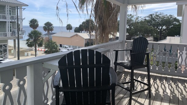 A covered porch with two Adirondack chairs, overlooking a beach and ocean view.
