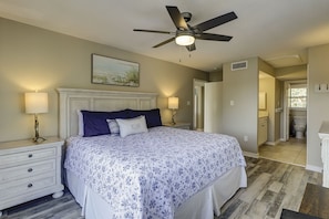 Une chambre à coucher avec un lit, des tables de chevet, un ventilateur de plafond et un tableau au mur.