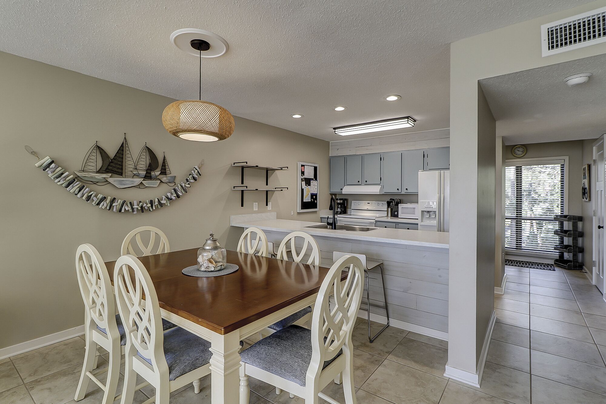 A modern kitchen with white cabinets, a central island, and a dining area with a wooden table and white chairs.