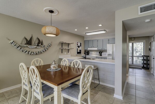 A modern kitchen with white cabinets, a central island, and a dining area with a wooden table and white chairs.