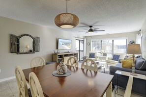 Un grand espace de vie comprenant une table à manger, des chaises, un canapé, un téléviseur et un ventilateur de plafond.