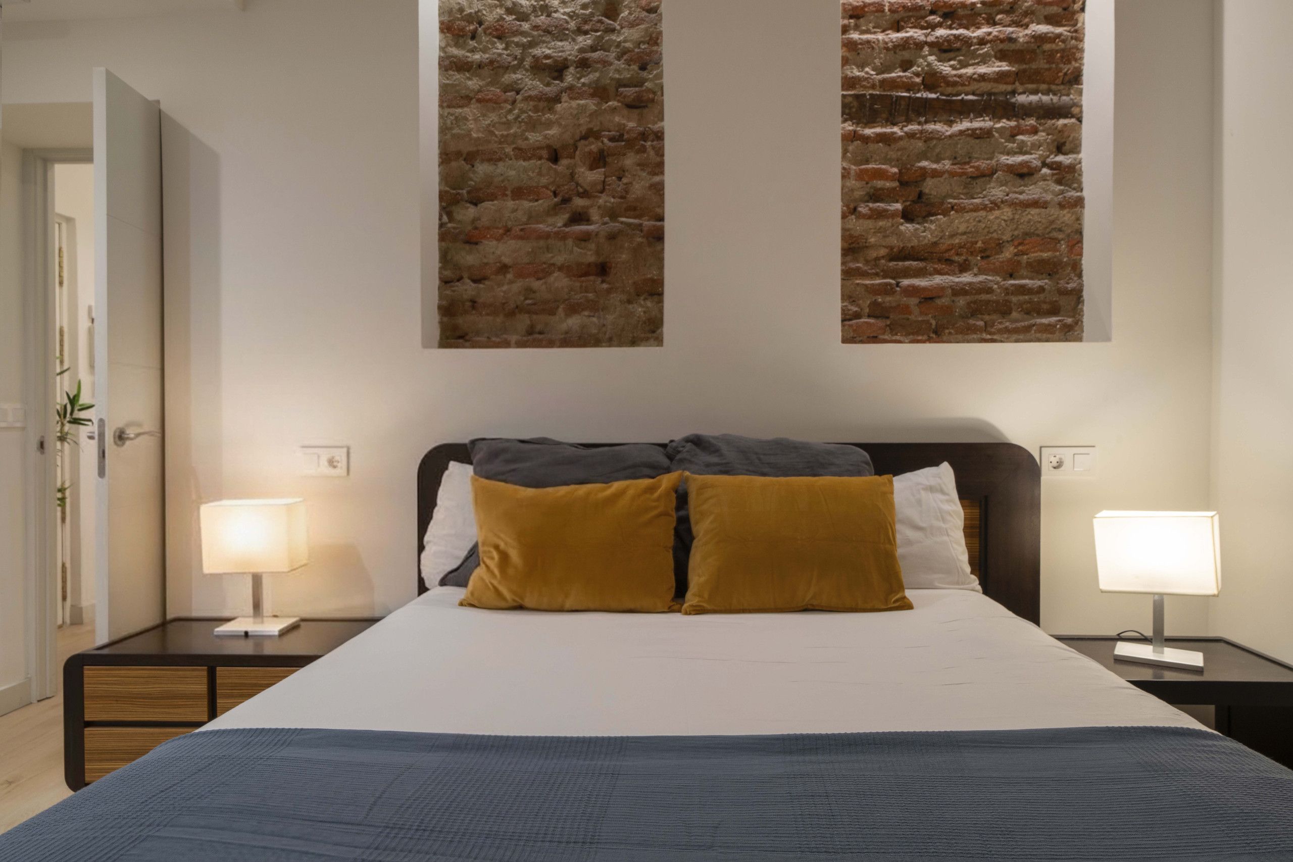 A hotel room with a large bed, two bedside lamps, a nightstand, and a wall with two textured panels.