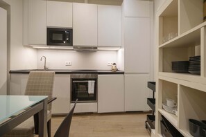 Eine moderne Küche mit weißen Schränken, einer Mikrowelle, einem Backofen und einem Glastisch.