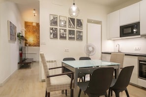 A modern kitchen with a microwave, a dining table with chairs, and a wall-mounted fan.
