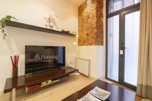 Ein modernes Wohnzimmer mit einem Flachbildfernseher auf einem Holzständer, einem Kamin, einer Wand mit Ziegeln und einer Schiebetür aus Glas.