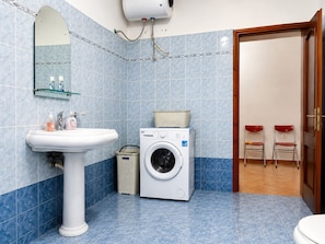 A bathroom with a sink, mirror, washing machine, and two red chairs.