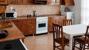 A kitchen with wooden cabinets, a stove, a microwave, and a dining area with chairs and a table. - Saranda 55  in Saranda, Albania. 10 min by Walking to City Center and Beach (Sarandë)