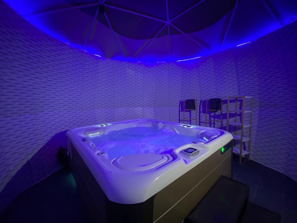 A modern spa room with a hot tub, a ceiling with a geometric design, and a brick wall.