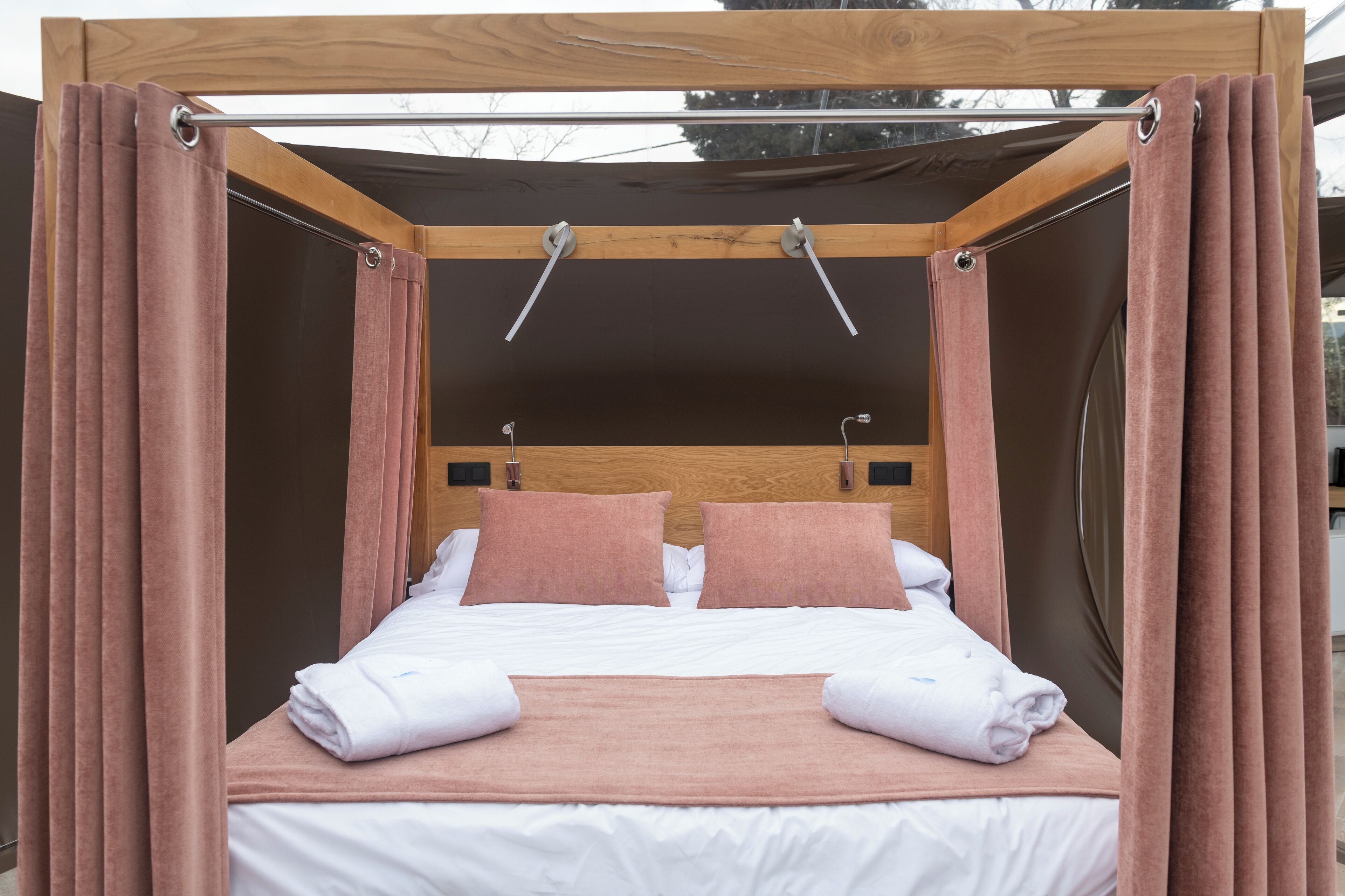 Una cama con dosel, ropa de cama blanca y almohadas rosas.