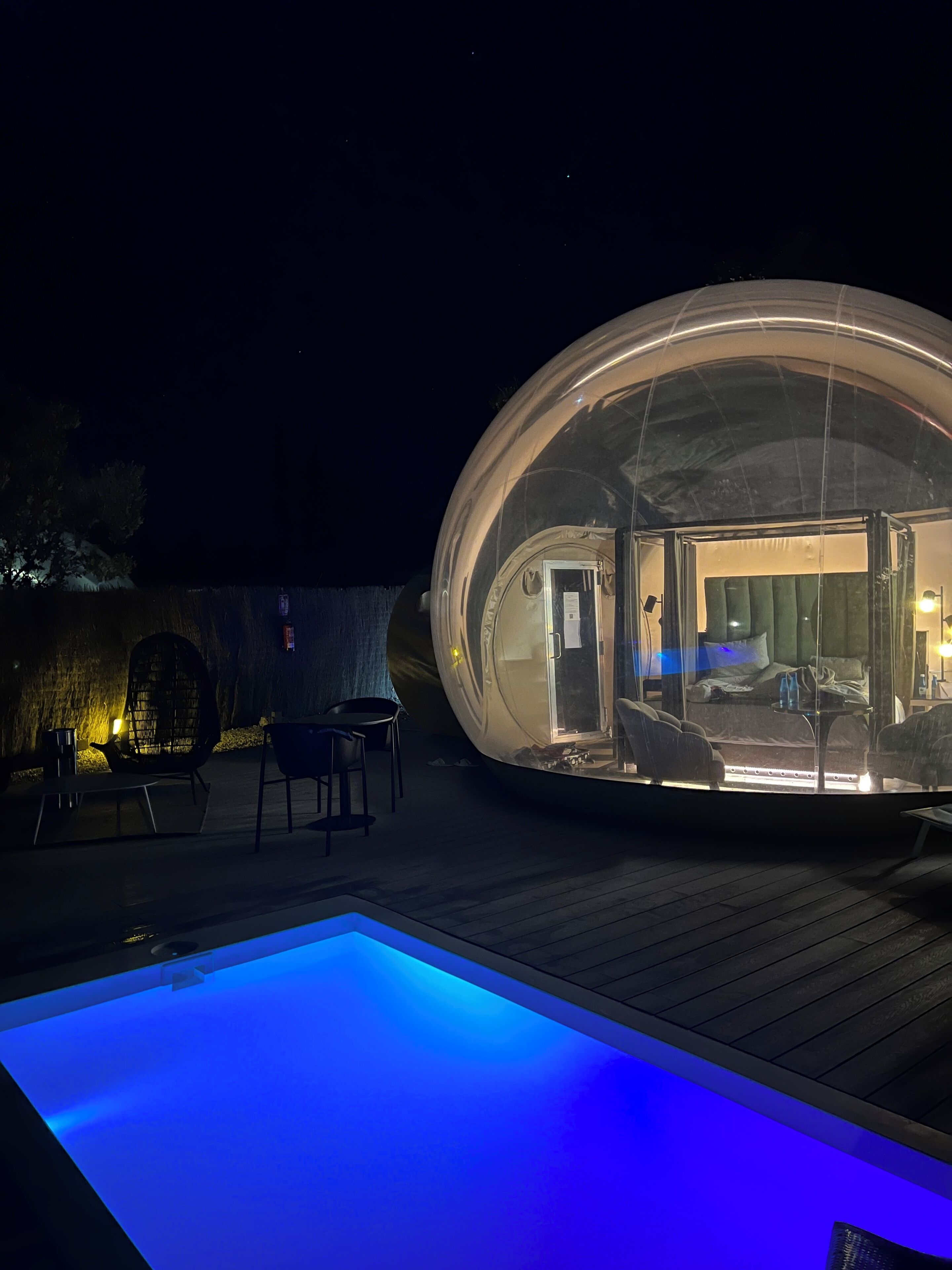 Una estructura esférica transparente con un área de asientos en su interior y una piscina.