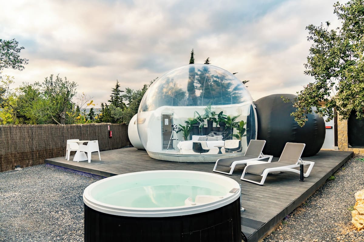 A transparent dome structure with seating inside, a hot tub, and lounge chairs outside.