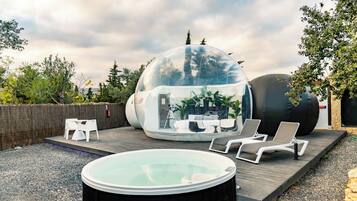 A transparent dome structure with seating inside, a hot tub, and lounge chairs outside.