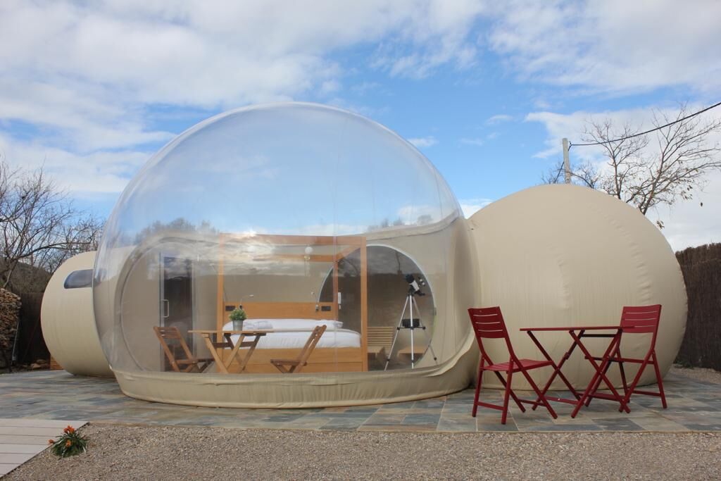 A transparent spherical structure with a bed, seating area, and a telescope.