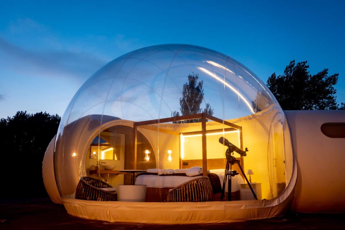 A transparent spherical structure with a bed, seating area, and a telescope.