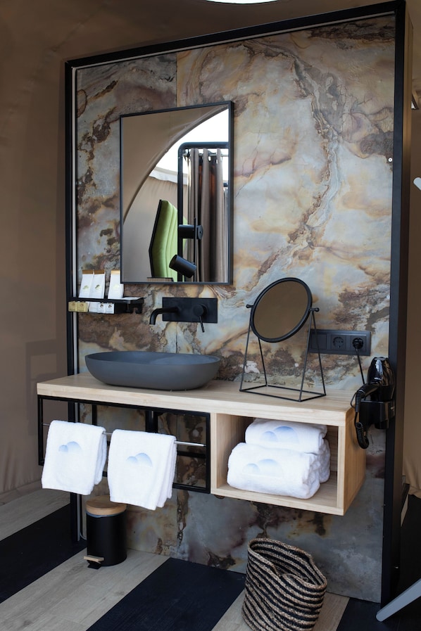 A bathroom with a marble backsplash, a round mirror, a vessel sink, and neatly folded towels on a shelf. - Hotel Zielo de Levante (Tirig)