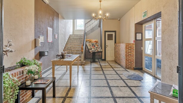 A hallway with a staircase, a chandelier, and a reception desk.