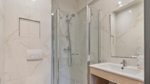 A modern bathroom with a glass-enclosed shower, a white toilet, a sink with a mirror above it, and a marble wall.
