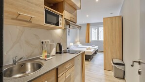 A modern kitchen with a built-in microwave, a sink, and wooden cabinets. There is a small trash bin and a window with curtains.