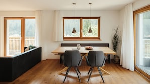 Un comedor con una mesa de madera, dos sillas, un banco y vistas amplias por ventanas grandes.
