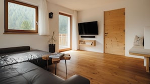 Una sala de estar moderna con un ventanal grande, un televisor de pantalla plana, una puerta de madera y un sofá.