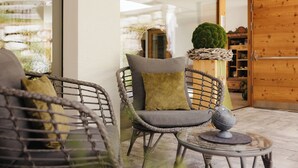 Sillas de mimbre con cojines, una mesa de vidrio con un objeto decorativo y una puerta de madera al fondo.