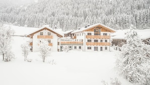 Una cabaña cubierta de nieve con varios pisos, balcones de madera y montañas al fondo.