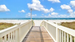 A wooden boardwalk leading to a beach with white railings and a clear blue sky. - Luxury Coastal Retreat | Heated Private Pool | Resort Style Amenities (Gulf Shores)