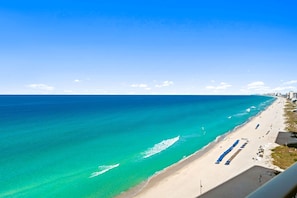 Une plage à l’eau turquoise et limpide, une longue étendue de sable et une rangée de parasols de plage bleus.